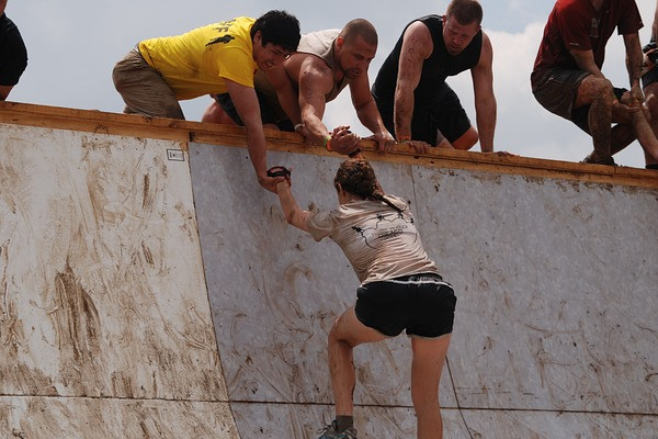 Teammitglieder helfen einem Mitglied dabei, eine hohe Mauer zu überwinden. Zusammenarbeit und Unterstützung